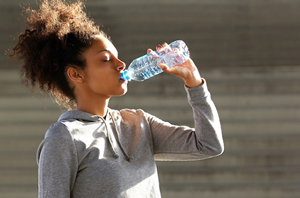 woman_stands_outside_in_sun_with_eyes_closed_drinking_water